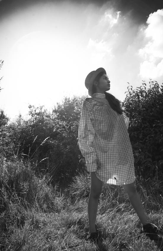 Girl standing in nature with oversized shirt and hat